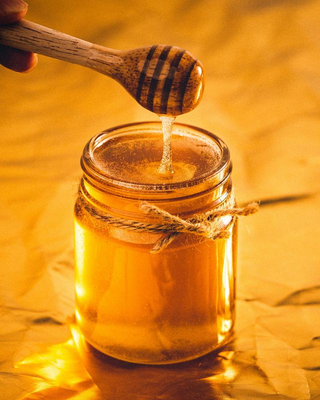 A glass jar of honey with a wooden dipper